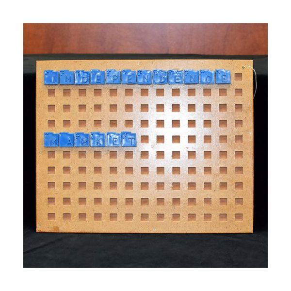 Rectangular wooden board with square holes and blue print/Braille begs that spell out "Independence Market".