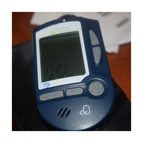 Blue Prodigy glucose monitor with LCD screen, gray rubberized control buttons, and front speaker.