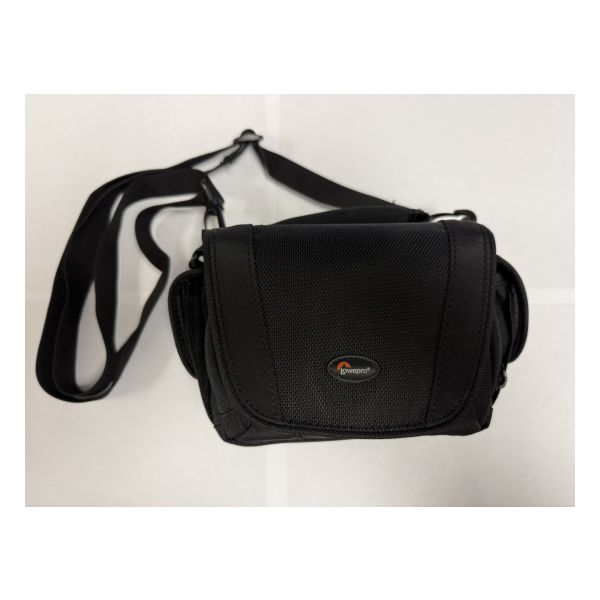 Top view of black nylon camera bag shows front flap, padded carrying handle on top, side pocket, and adjustable carrying strap.